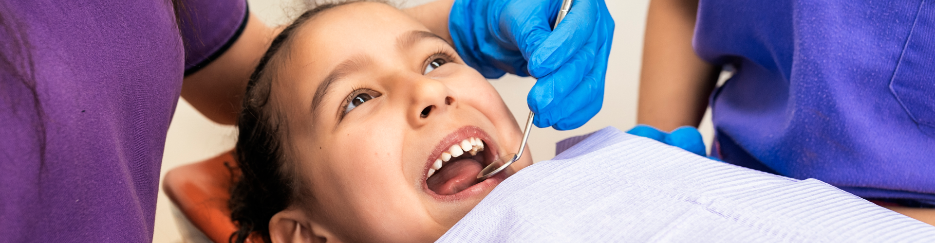 Gloved hands using dental tools in girl's mouth.